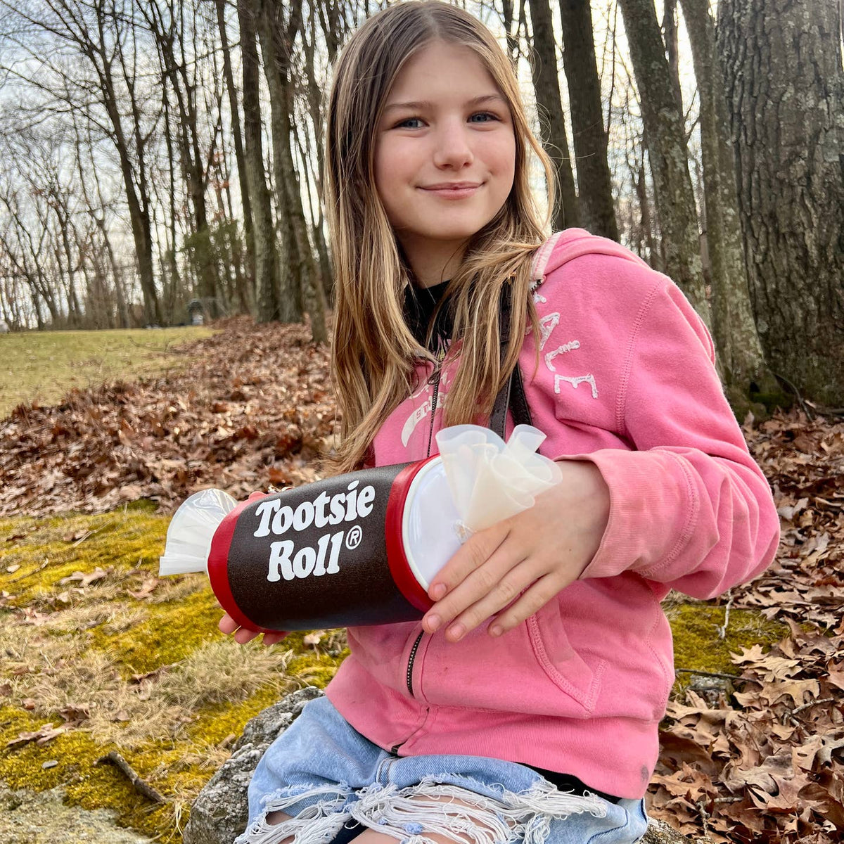 Girl holding a large Tootsie Roll candy in a forest setting