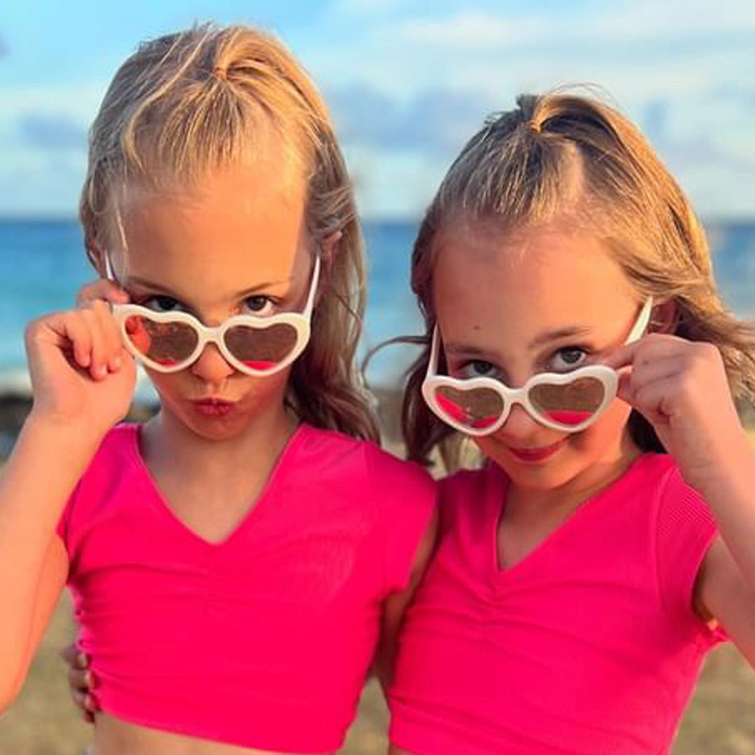 Two children wearing heart-shaped sunglasses on a beach.