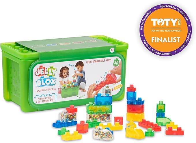The product image displays the Jelly Blox Stash 'n' Stack toy set by Continuum Games, featuring a purple circular badge in the top right corner indicating it as a Toy of the Year (TOTY) Awards 2025 Finalist.
It includes a bright green rectangular storage box with a translucent lid and a product label on the front, alongside several colorful, translucent squishy building blocks and sensory pieces arranged in front of it on a white background.