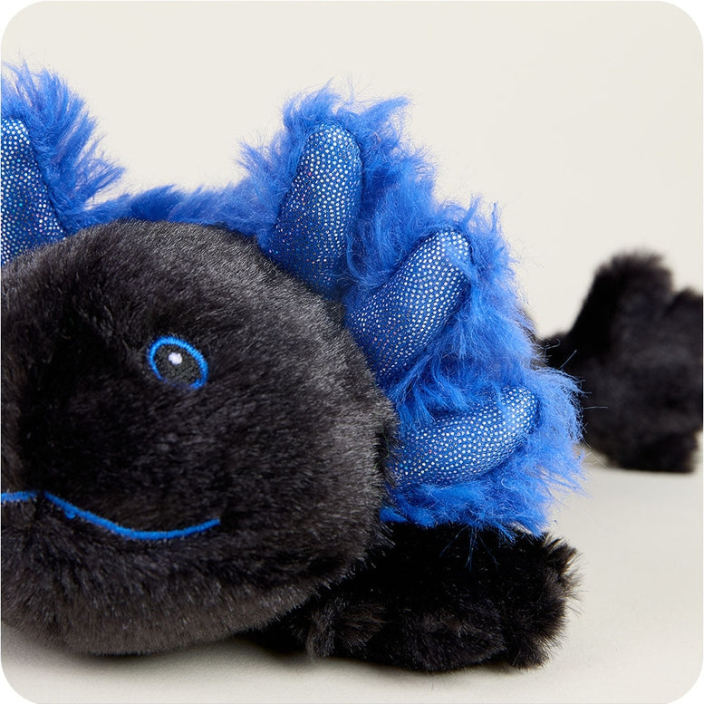 A low-angle close-up of a black and blue Axolotl Junior plush toy by Warmies, highlighting its soft black face, smiling expression, and vibrant blue external gills.
