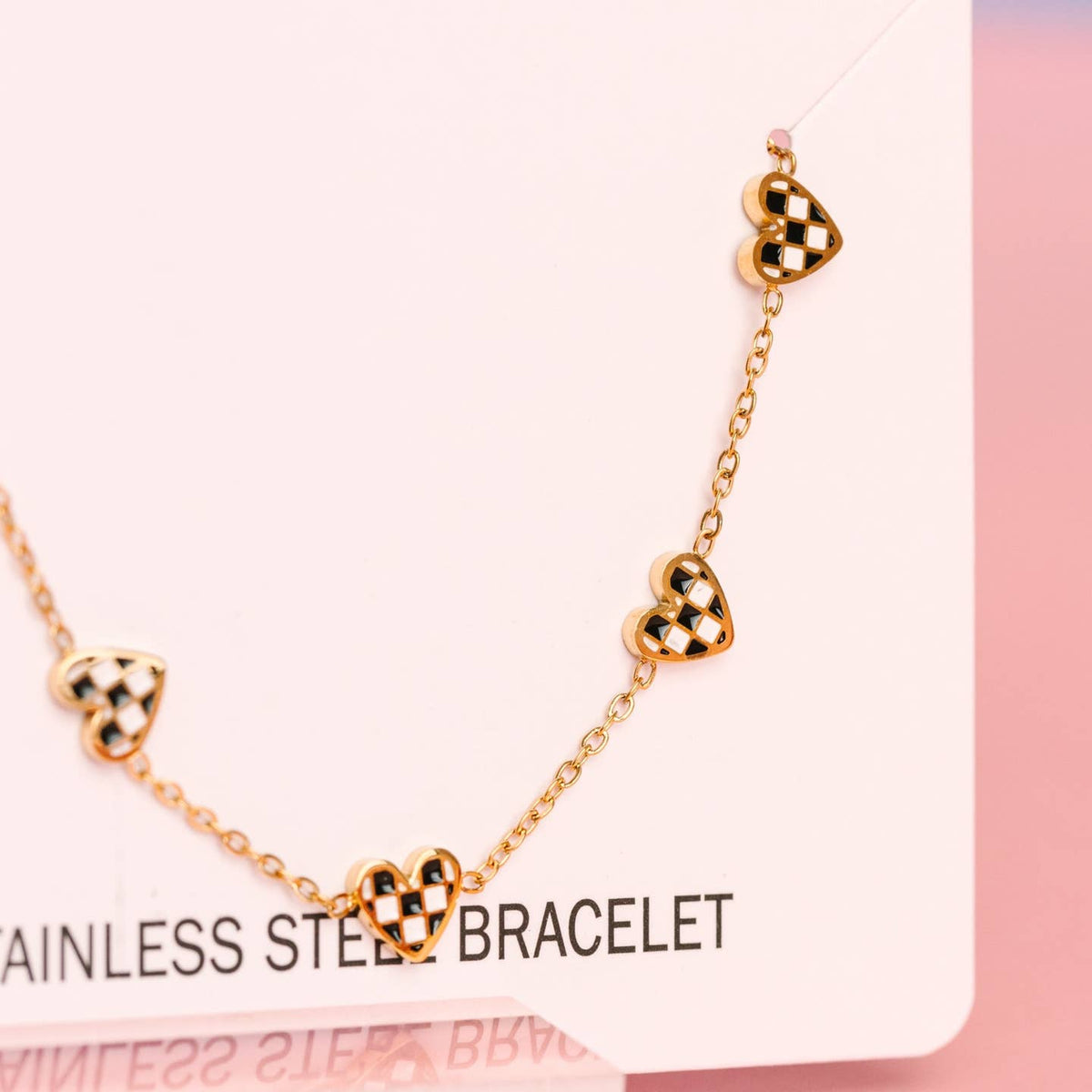 Gold bracelet with heart-shaped charms on a pink background