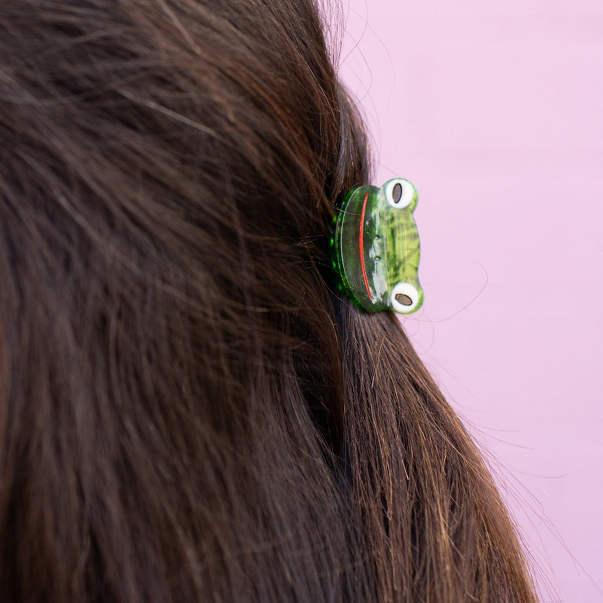 Green hair clip on a person's hair against a pink background