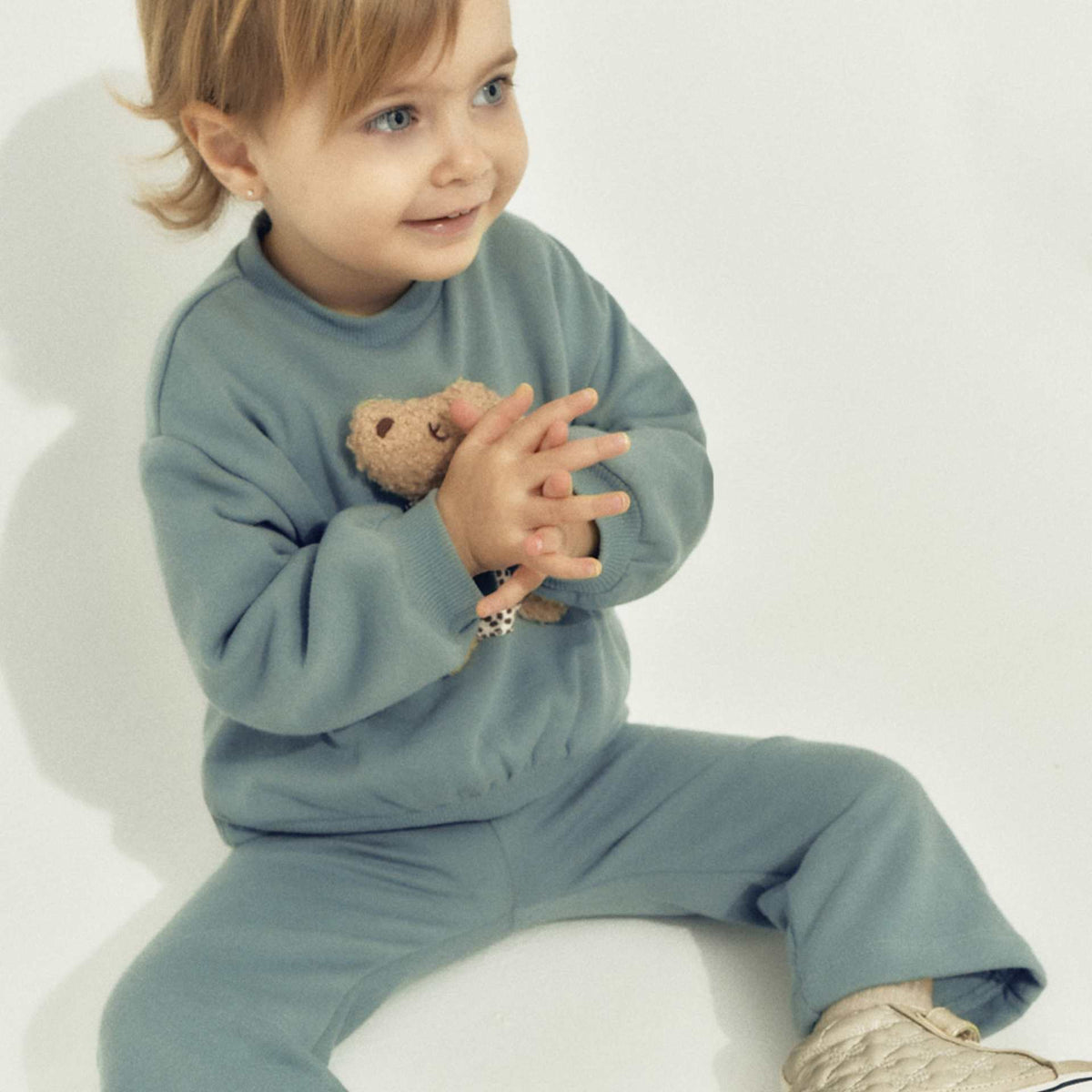 Child wearing a blue outfit holding a teddy bear on a white background