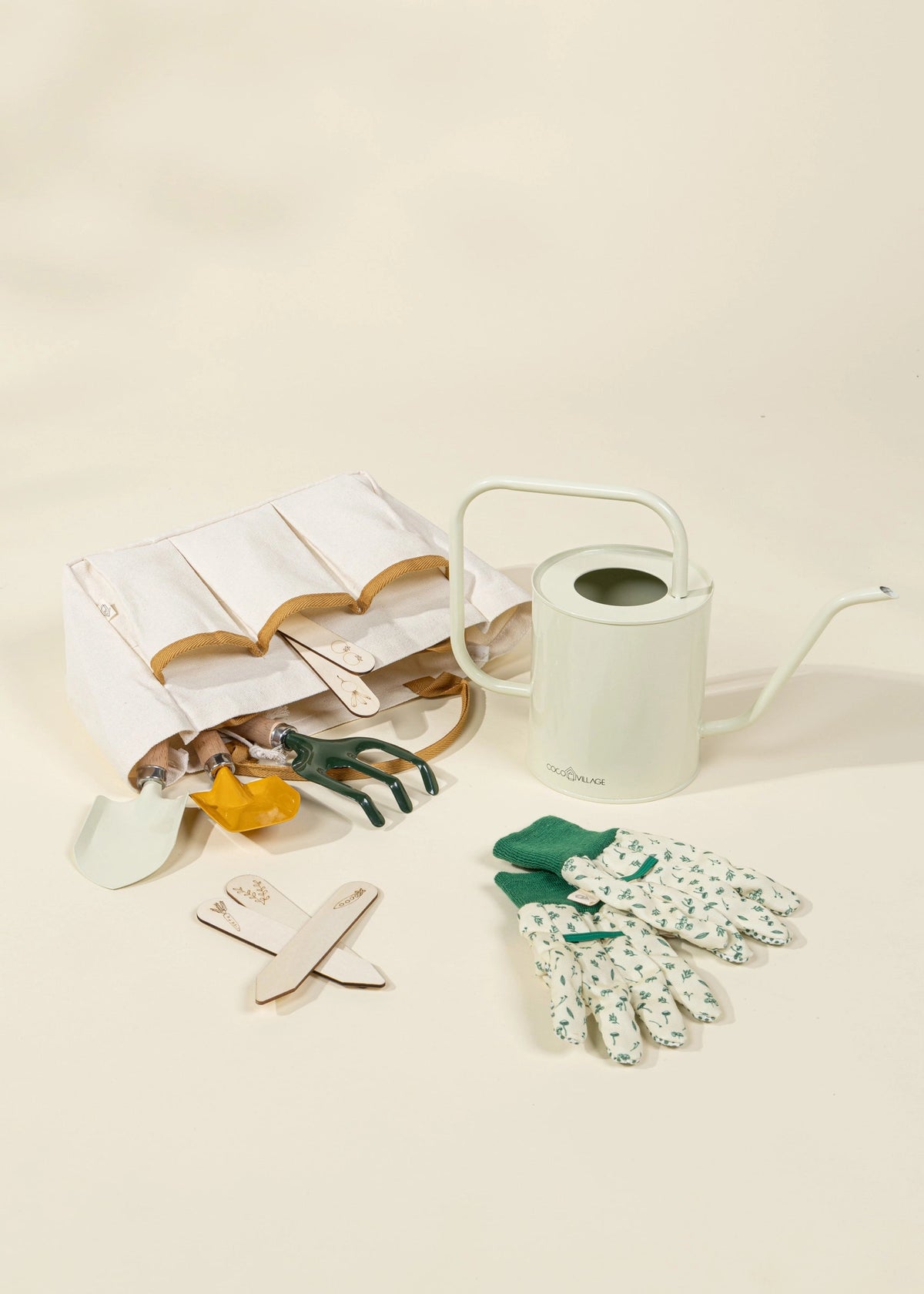 Gardening tools including a watering can, gloves, trowel, and small shovel on a beige background.