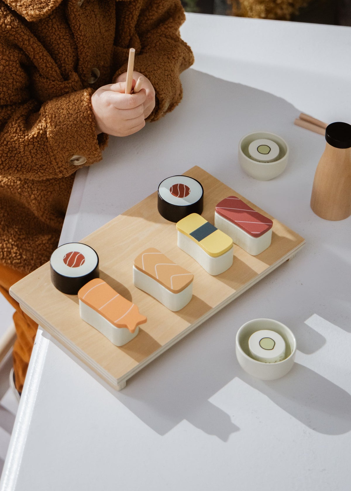 Child playing with a wooden toy set of sushi on a white table.