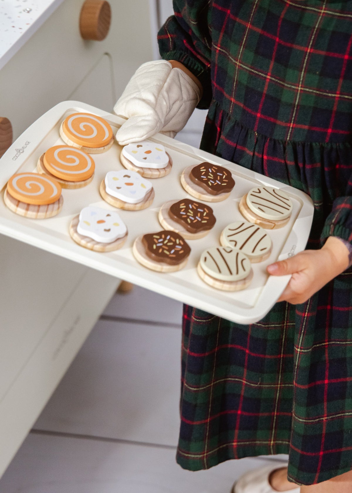 Person holding a tray of decorated cookies in a kitchen setting