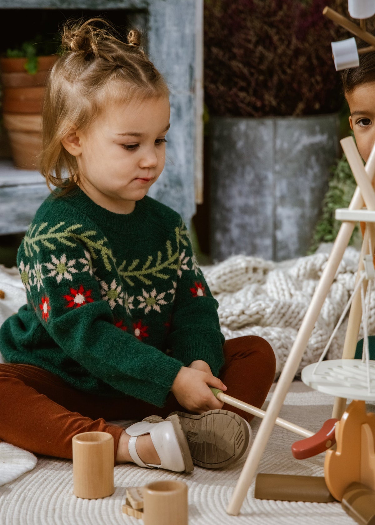 Child in a green sweater playing with wooden toys on a blanket
