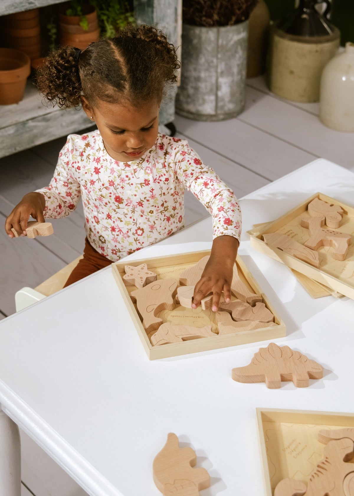 Child playing with wooden dinosaur toys on a white table outdoors.