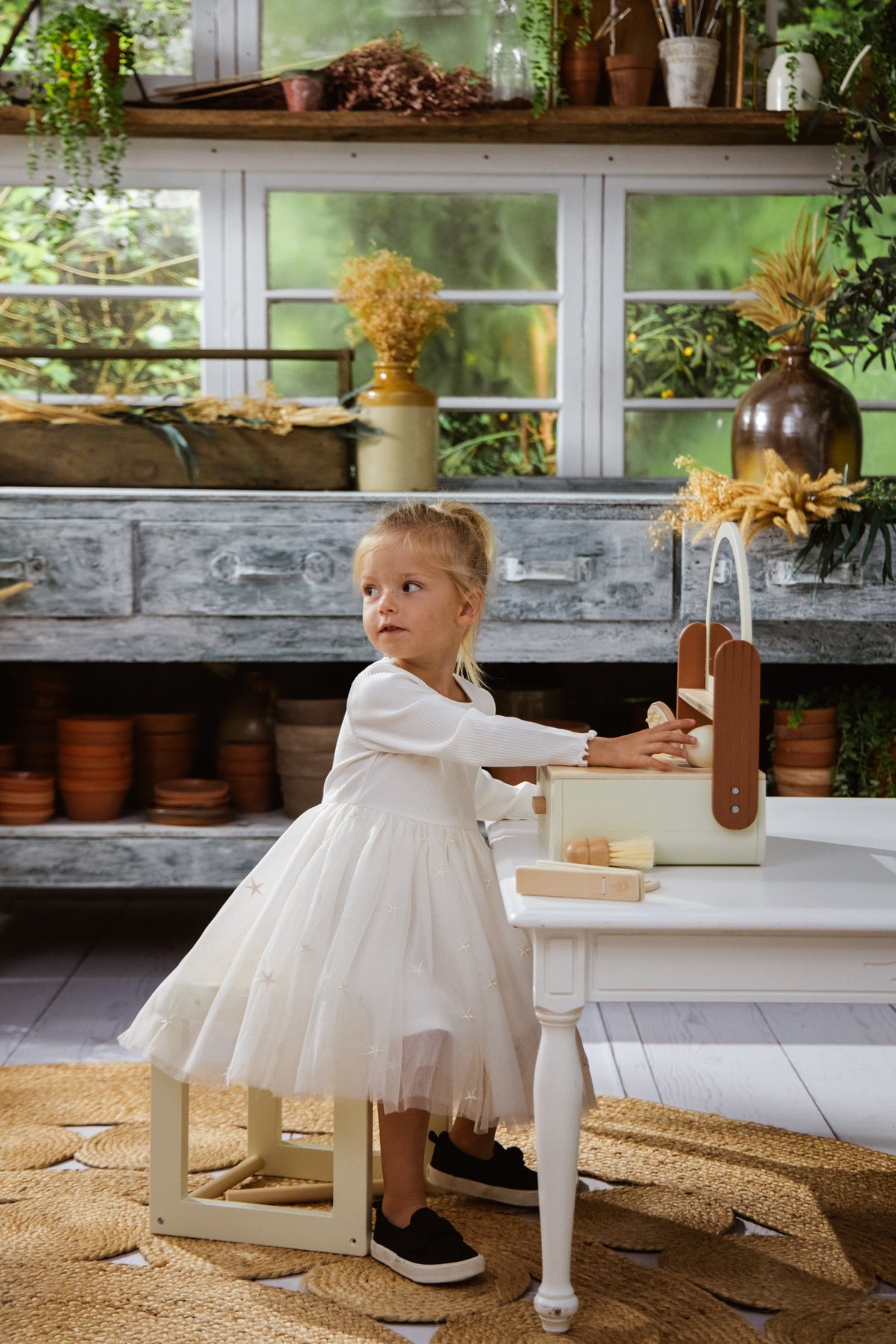 Young girl in a white dress playing with a wooden toy in a rustic kitchen.