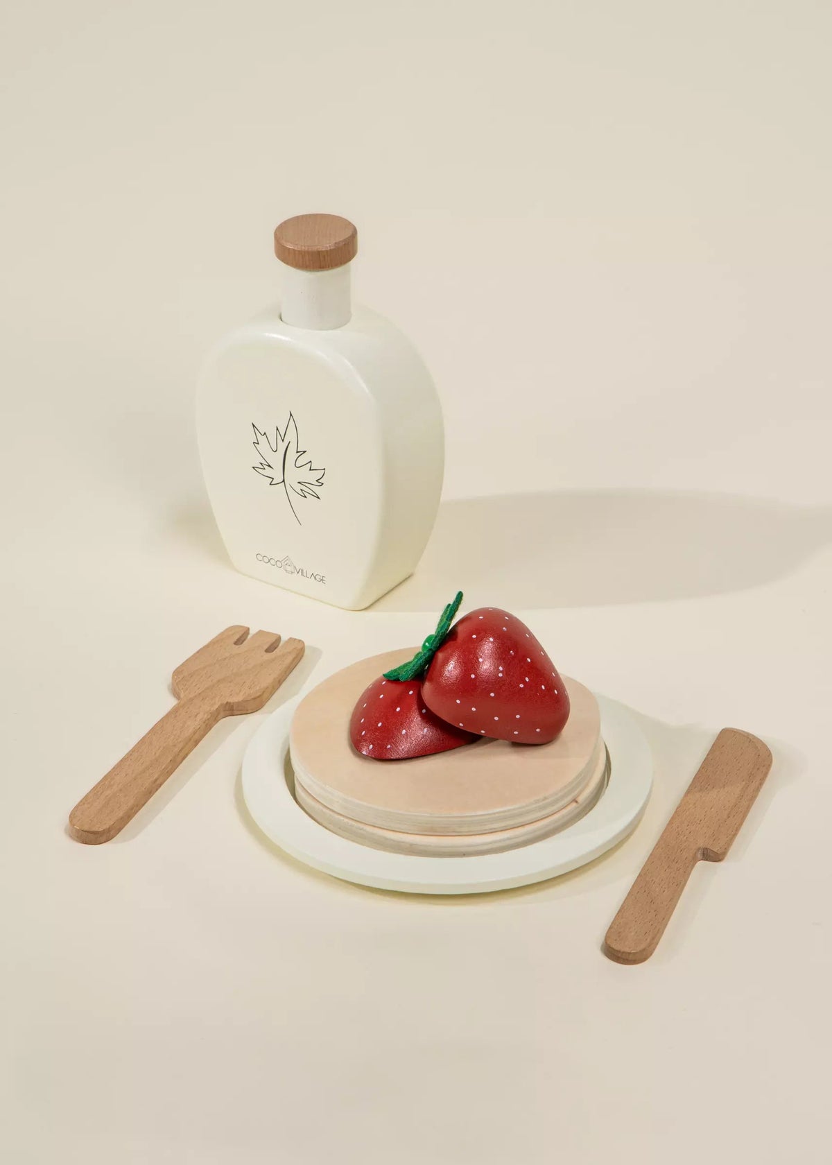 Set of wooden toys including a bottle, knife, fork, and two red strawberries on a beige background