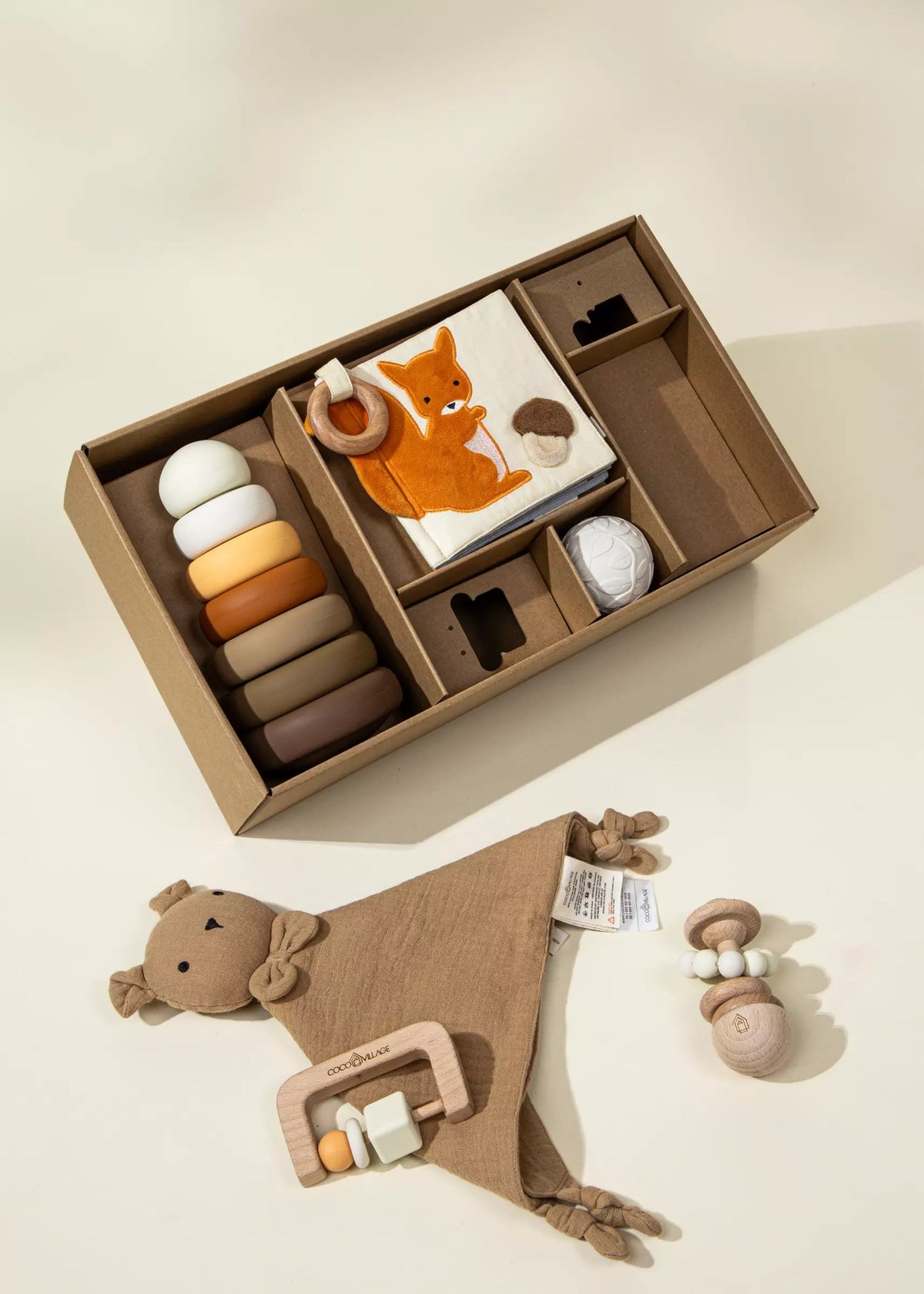 Set of baby toys including a rattle, book, and soft blanket in a box on a light surface.