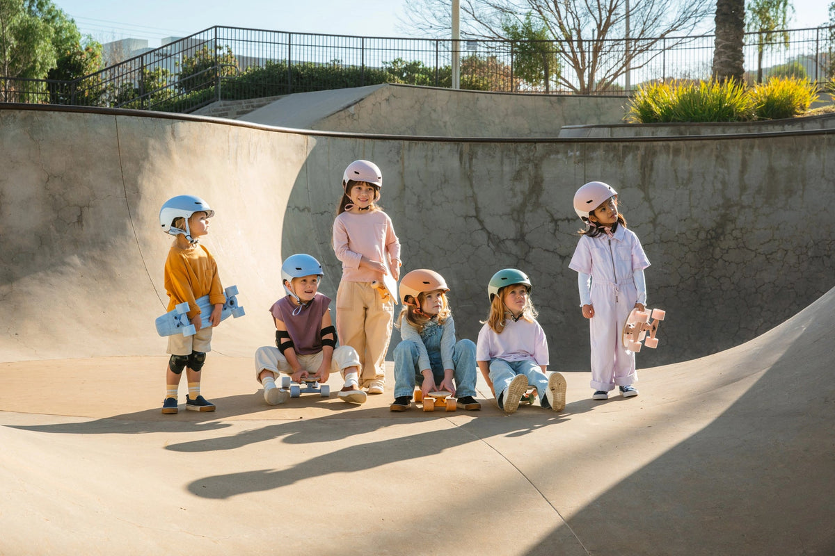 Children with skateboards and safety gear at a skate park.