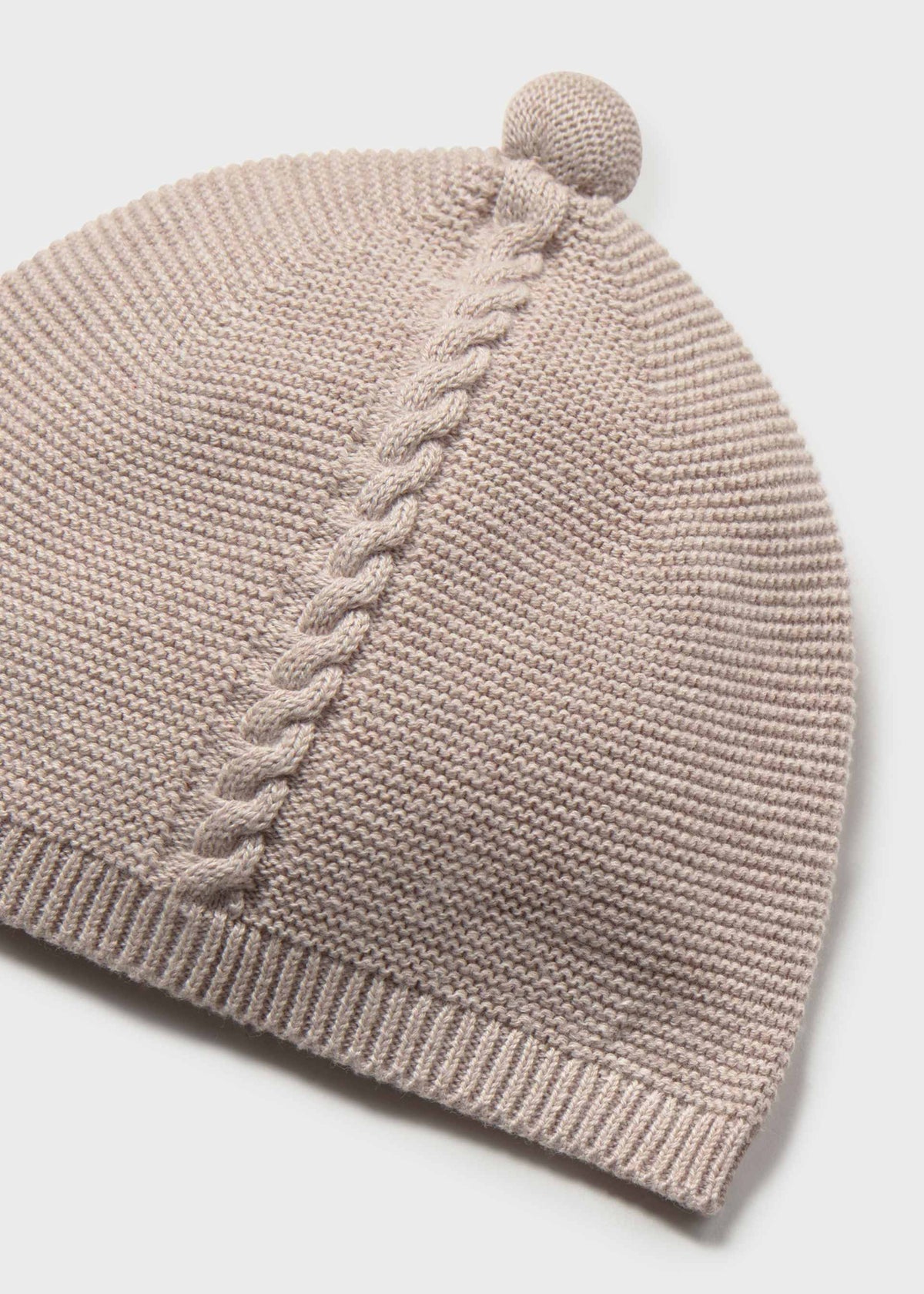 A close-up of a light taupe knit beanie hat featuring a vertical cable-knit pattern and a matching pom-pom on top, set against a clean white background.