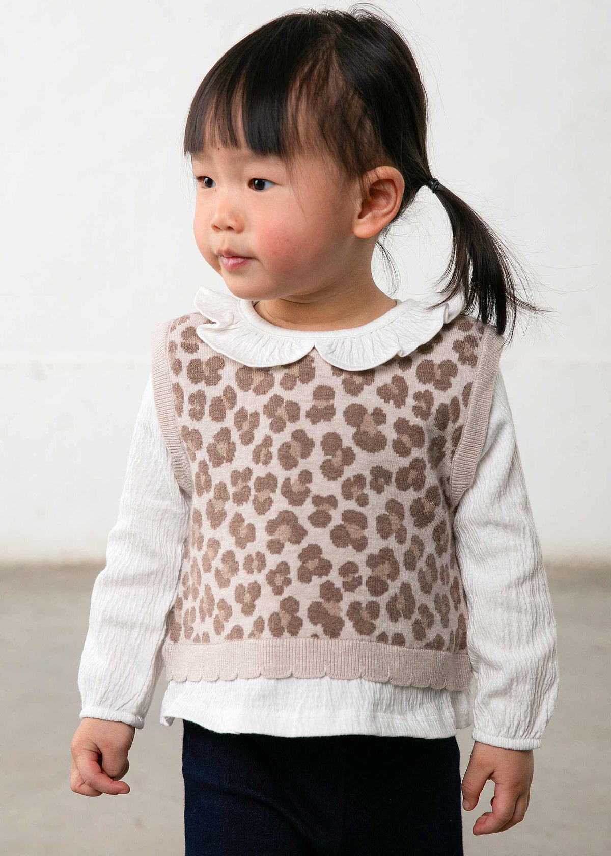 Child wearing a patterned vest over a white shirt with a plain background