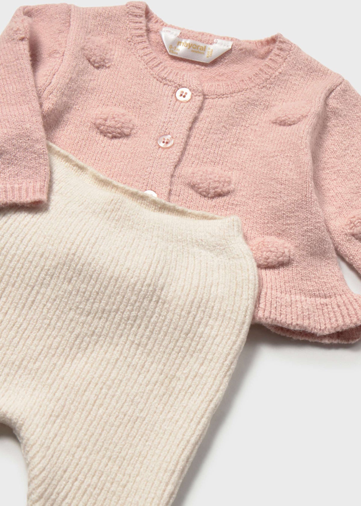 Pink knitted cardigan and beige pants on a white background