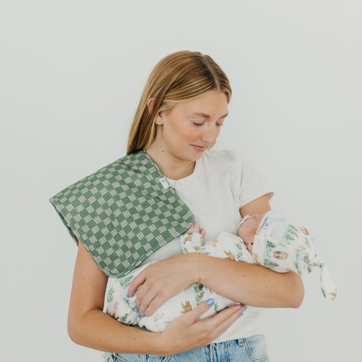 Woman holding a baby wrapped in a green and white checkered blanket against a plain background