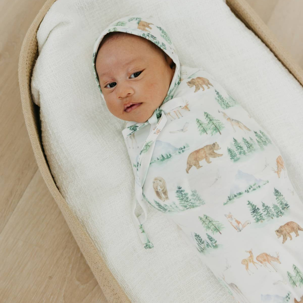 Newborn baby swaddled in a forest-themed blanket on a soft surface