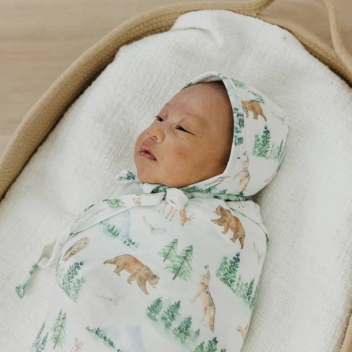 Newborn baby wrapped in a forest-themed swaddle blanket with a hood.
