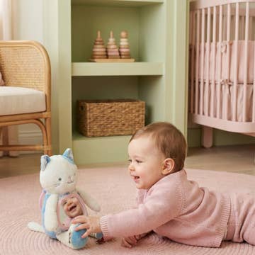 Baby playing with a soft toy on a pink rug in a nursery.