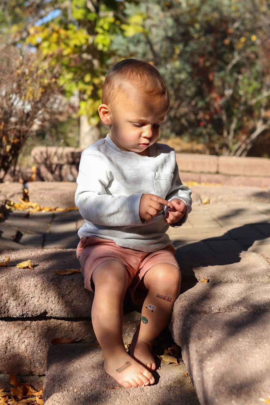 Child sitting on a stone ledge outdoors with trees in the background