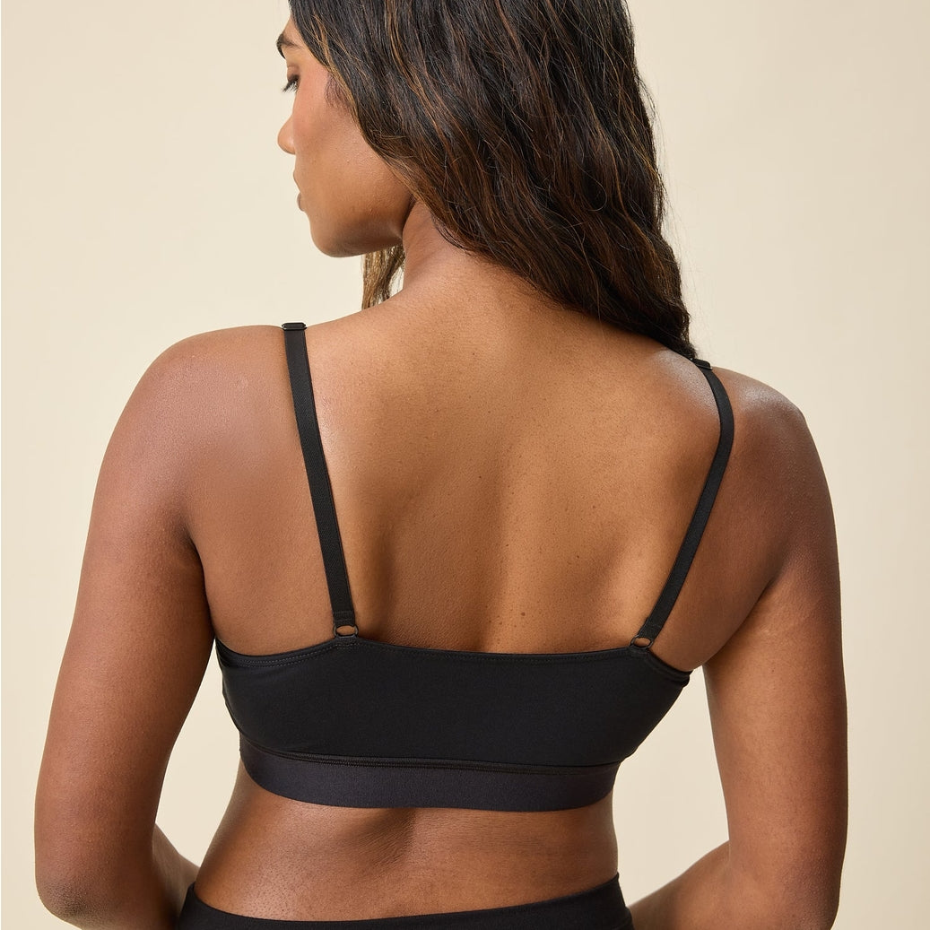 A woman shown from the back wearing a black sports bra and matching black bottoms against a plain beige studio background.