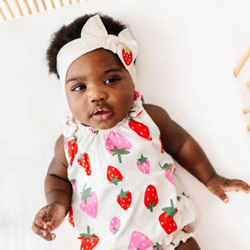 Baby wearing a white romper with strawberry pattern and a matching headband.