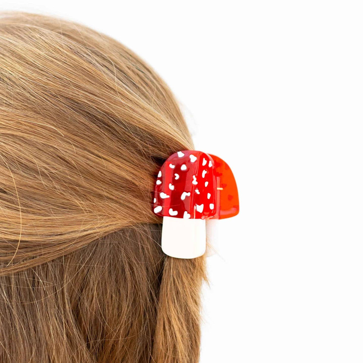 Red mushroom-shaped hair clip on a person's hair against a white background
