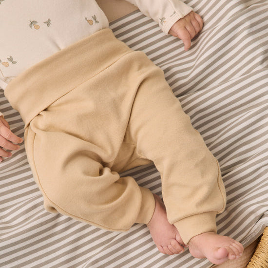 A baby lying on a beige and white striped blanket, wearing beige knit pants and a cream long-sleeve top with small floral prints.