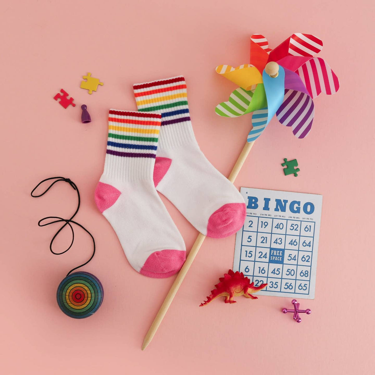 Colorful socks with rainbow stripes, a pinwheel, and a bingo card on a pink background