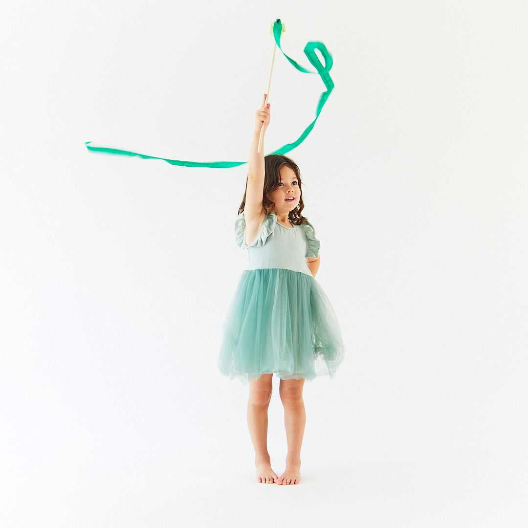 Young girl in a light green dress holding a green ribbon against a white background