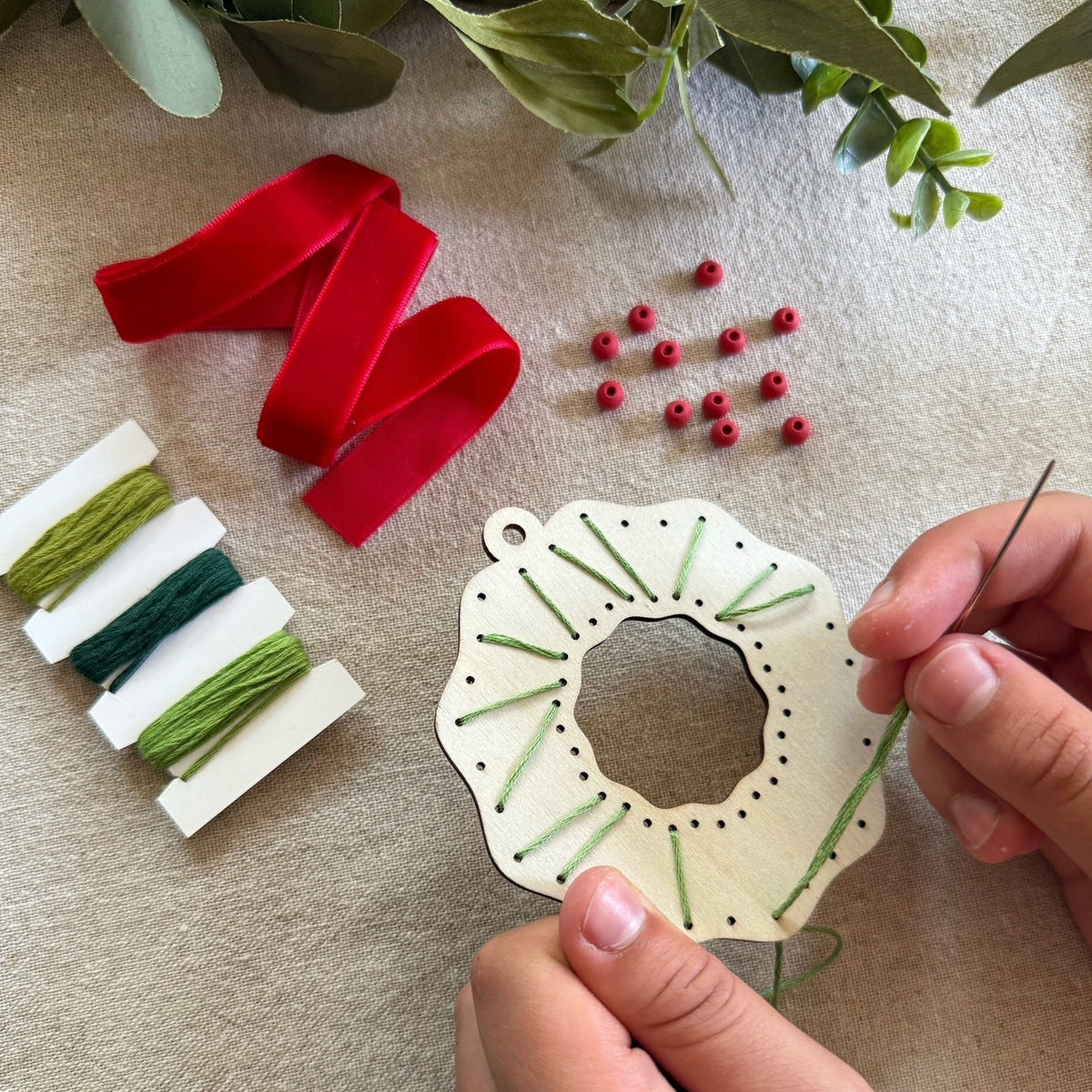 Handmade ornament with green embroidery on a beige surface with red ribbon and berries.