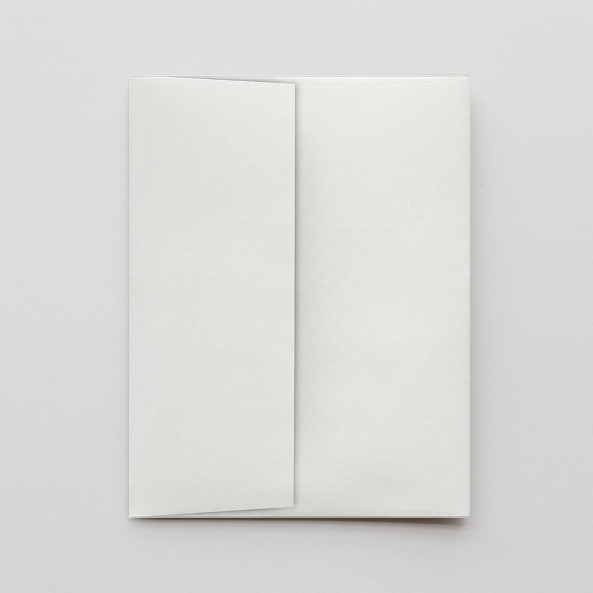 A blank white envelope with a closed flap, photographed flat against a light gray background.