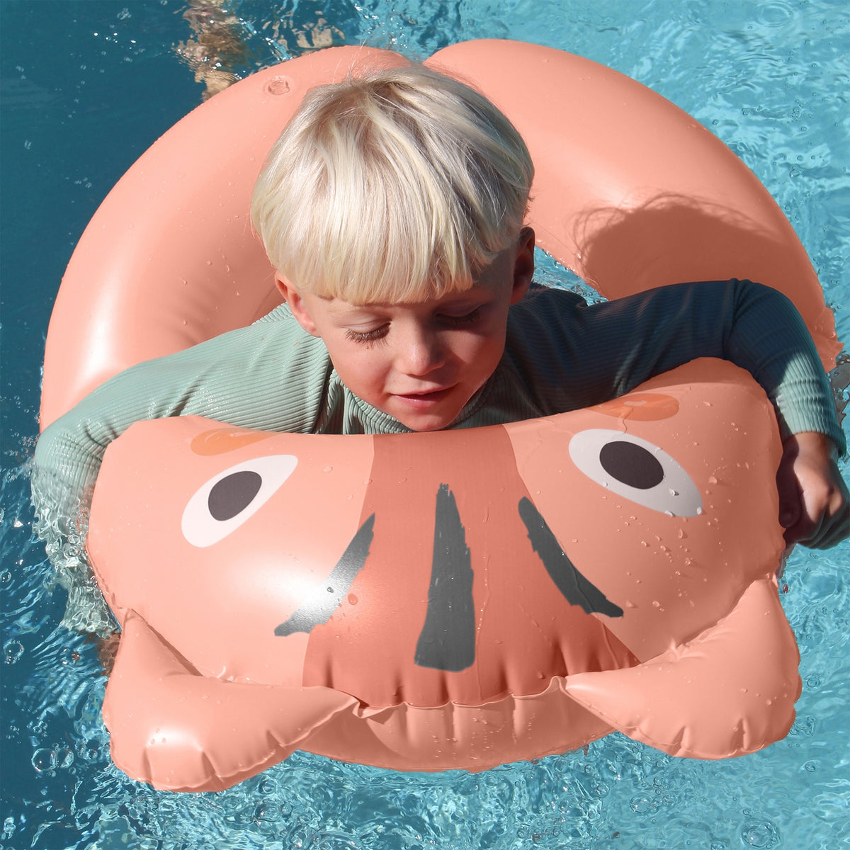 Child on a pink inflatable animal float in a pool