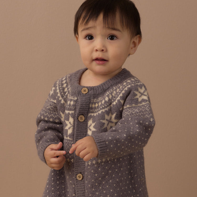 A baby wearing a gray knit cardigan and matching knit pants with cream-colored snowflake patterns.