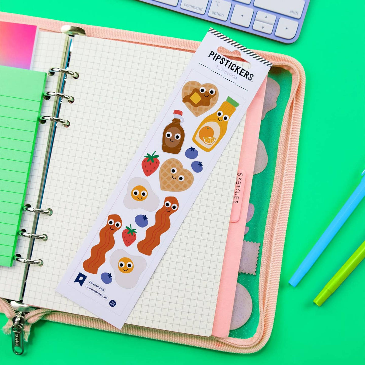 Pack of Pipstickers with cartoon food designs on a notebook with pens and a keyboard in the background.
