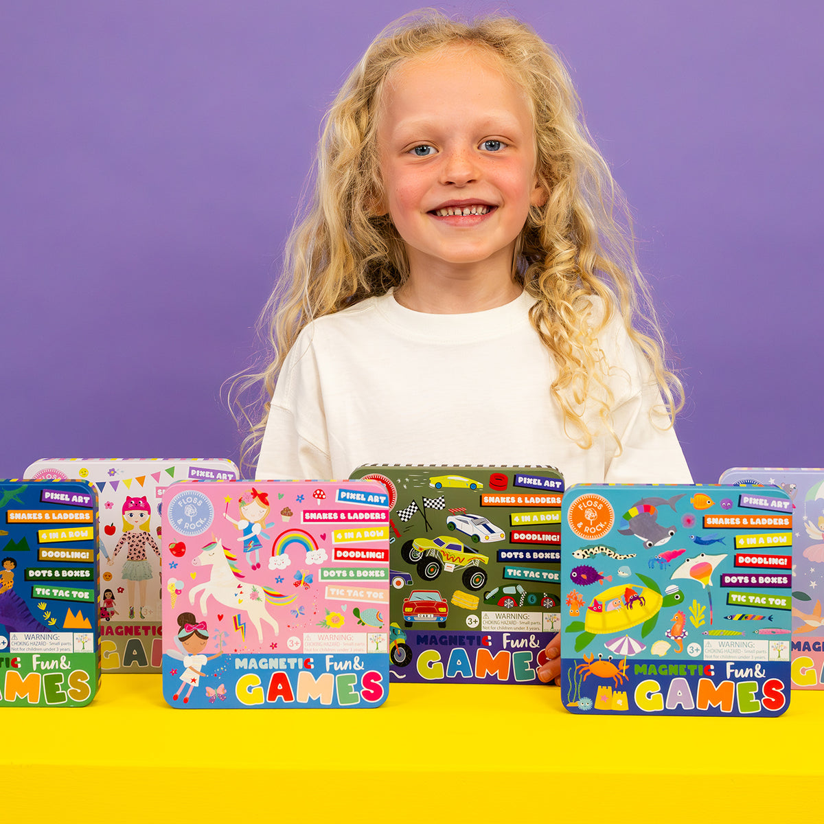 Young girl with a row of colorful game boxes on a yellow table against a purple background