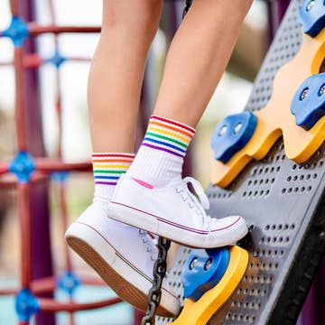 Children's feet wearing white sneakers and rainbow socks on a playground.
