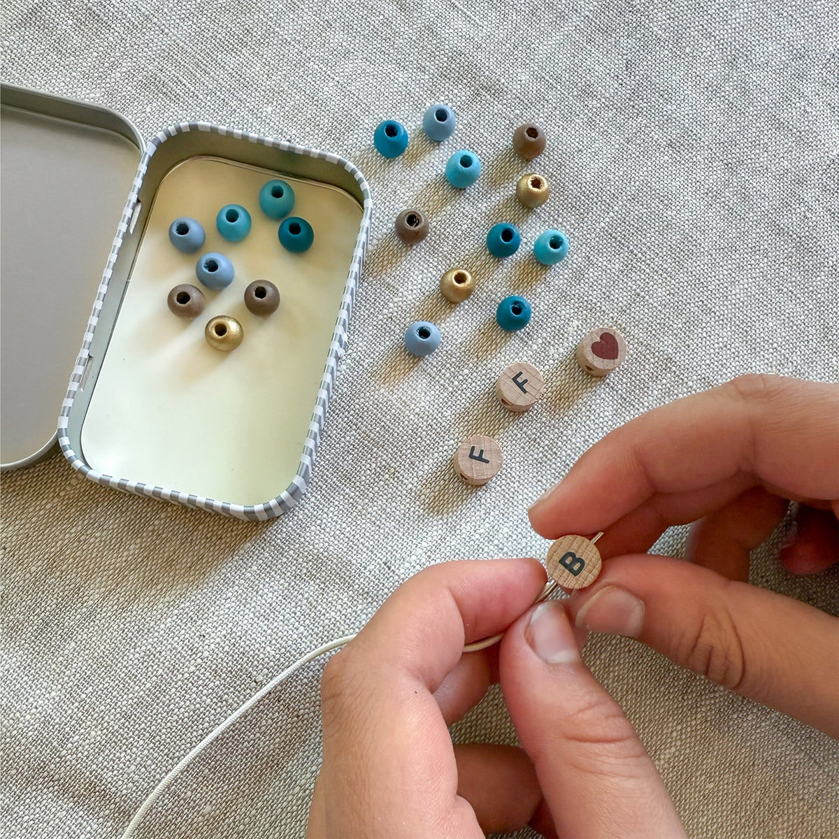 Person assembling small wooden beads with letters on a textured surface
