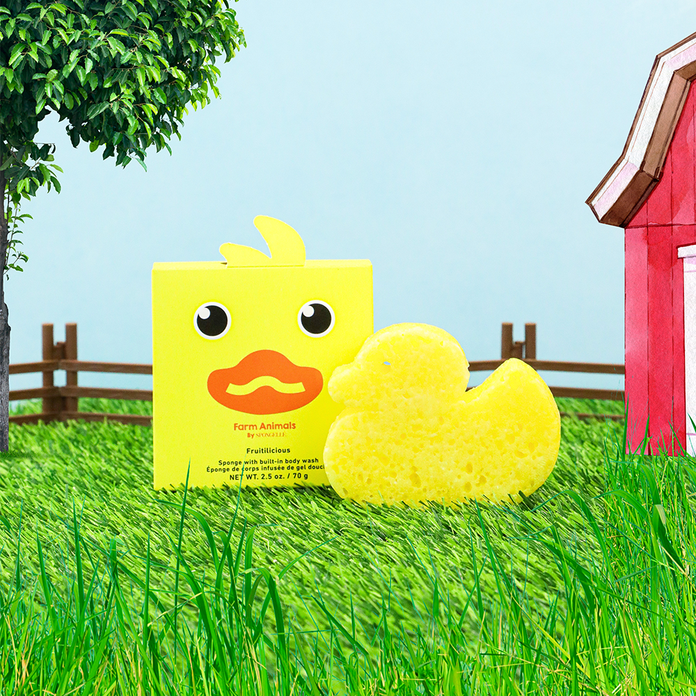 Yellow chick toy with packaging on grass in front of a red barn and green trees