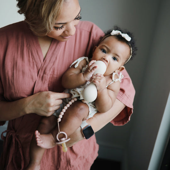 Woman holding a baby wearing a pink outfit with a teething ring.