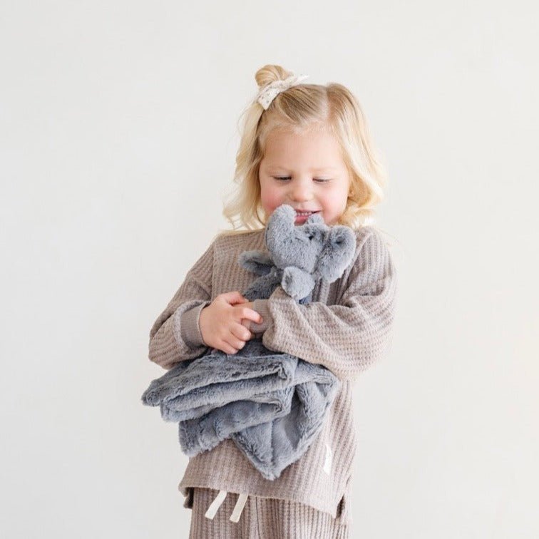 Child holding a gray blanket and toy on a plain background