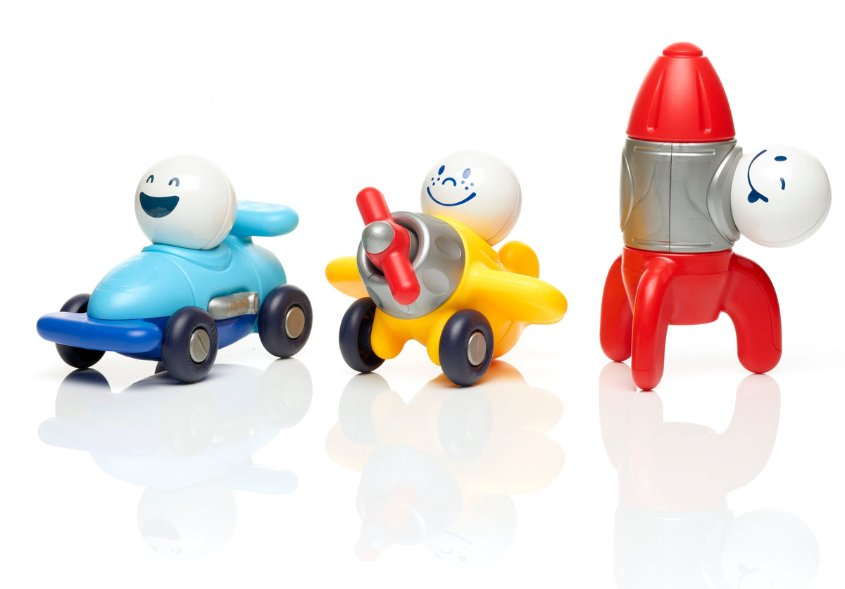 Three colorful plastic toy vehicles with smiling cartoon faces: a blue race car, a yellow airplane, and a red rocket ship, arranged on a white reflective surface against a white background.