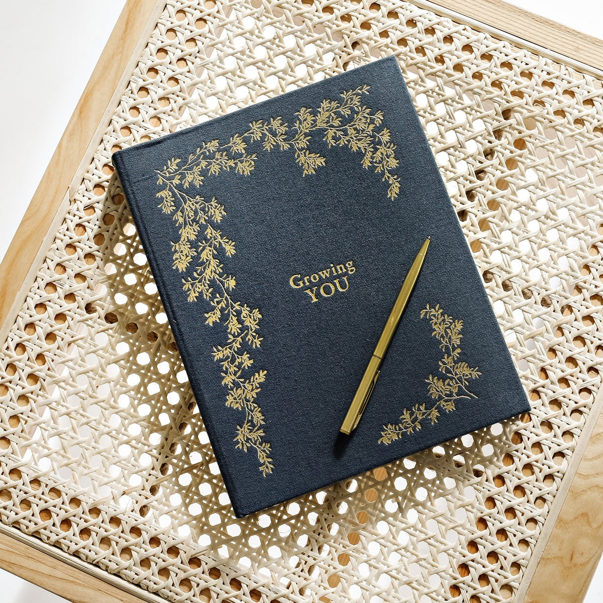 Blue notebook with gold text and floral design on a wicker surface