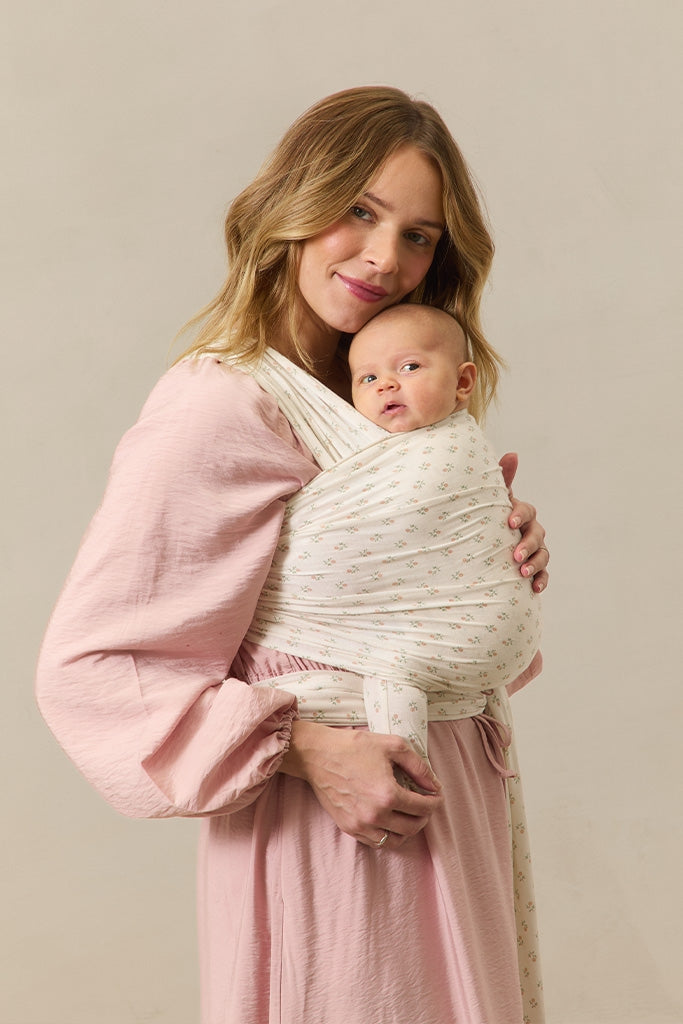 Woman holding a baby wrapped in a white wrap against a beige background