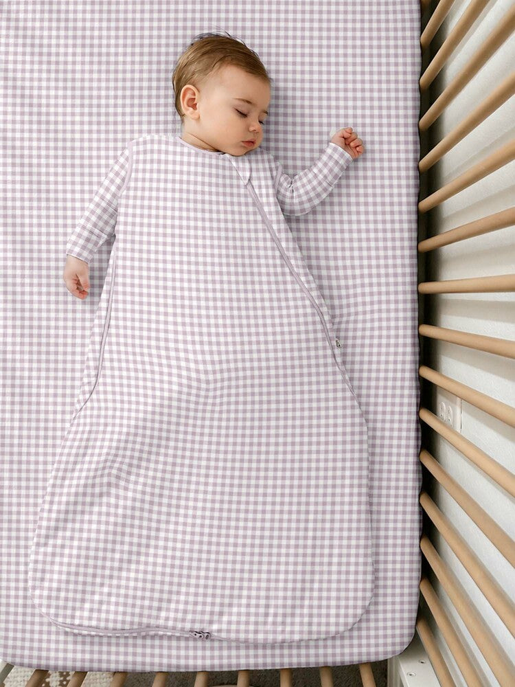 A baby sleeping in a günamüna Sleep Sack in a charming pink-and-white gingham pattern featuring a convenient diagonal zipper