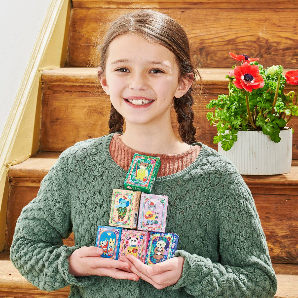 Young girl holding colorful cards on wooden steps with a potted plant in the background
