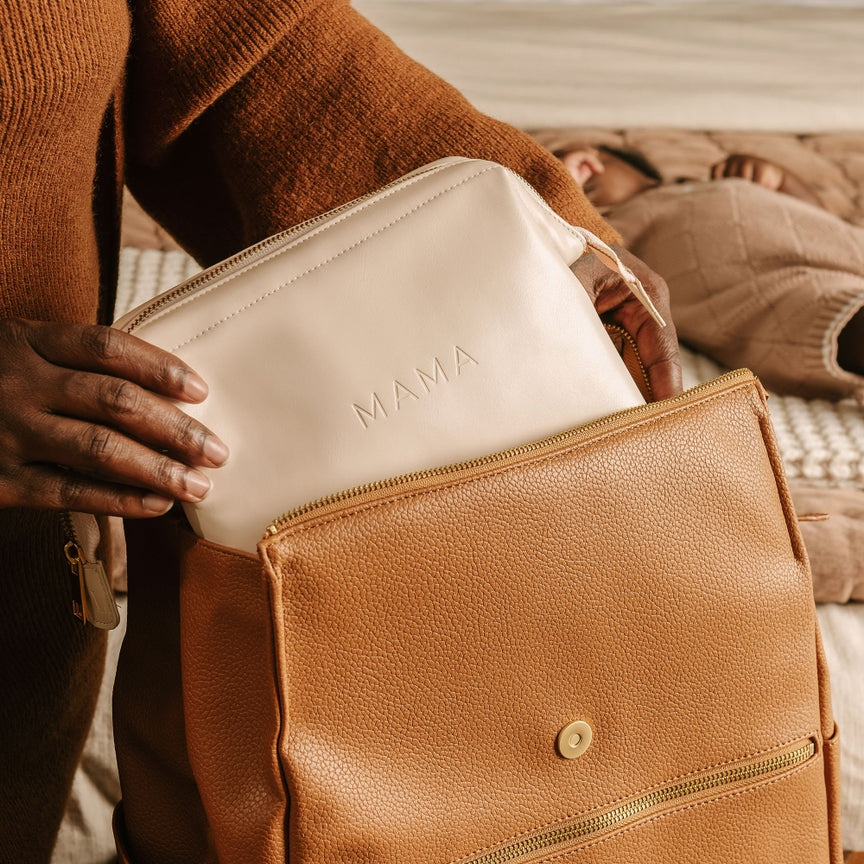 Person holding a white pouch with 'MAMA' printed on it, placed inside a brown leather bag.