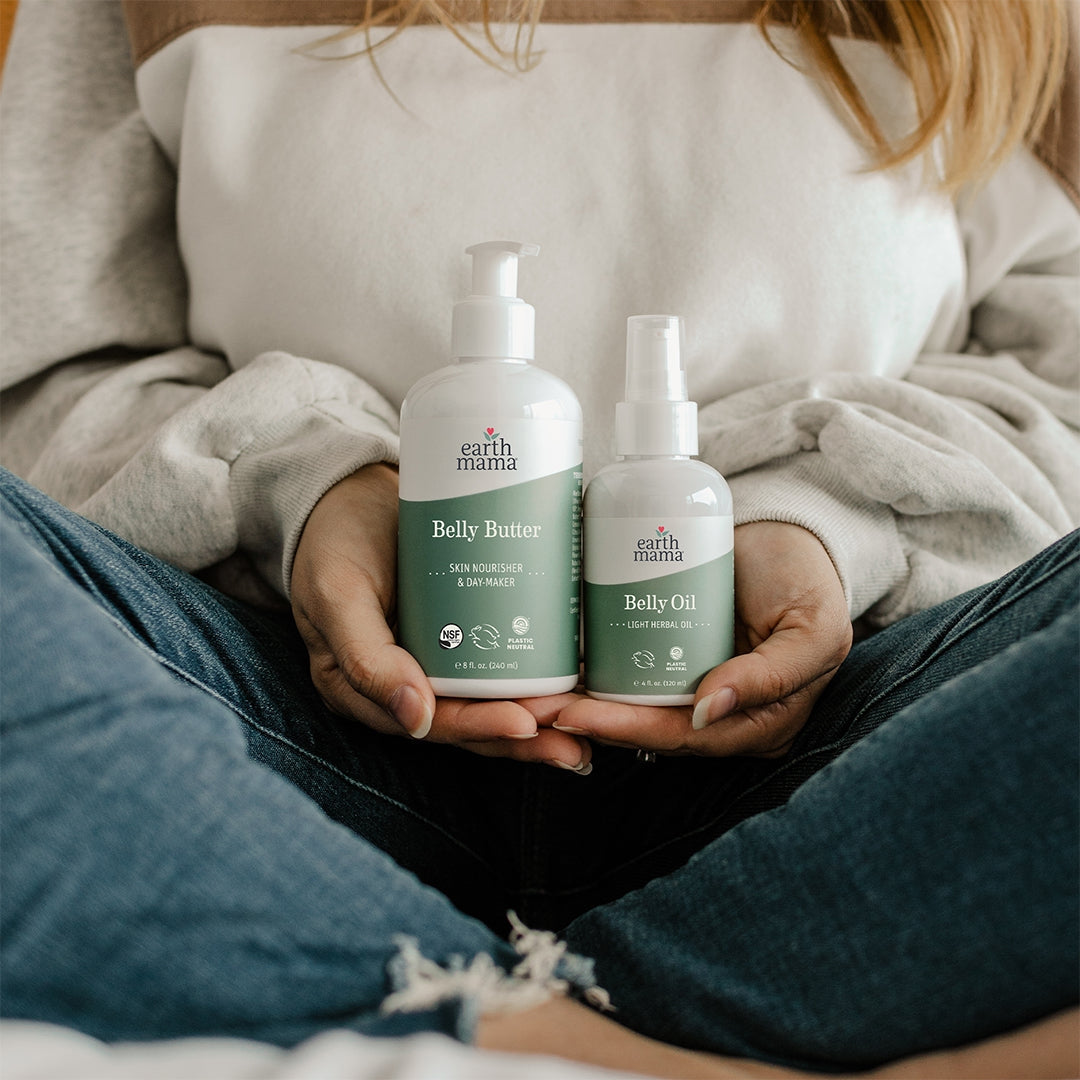 Person holding Earth Mama Belly Butter and Belly Oil bottles.