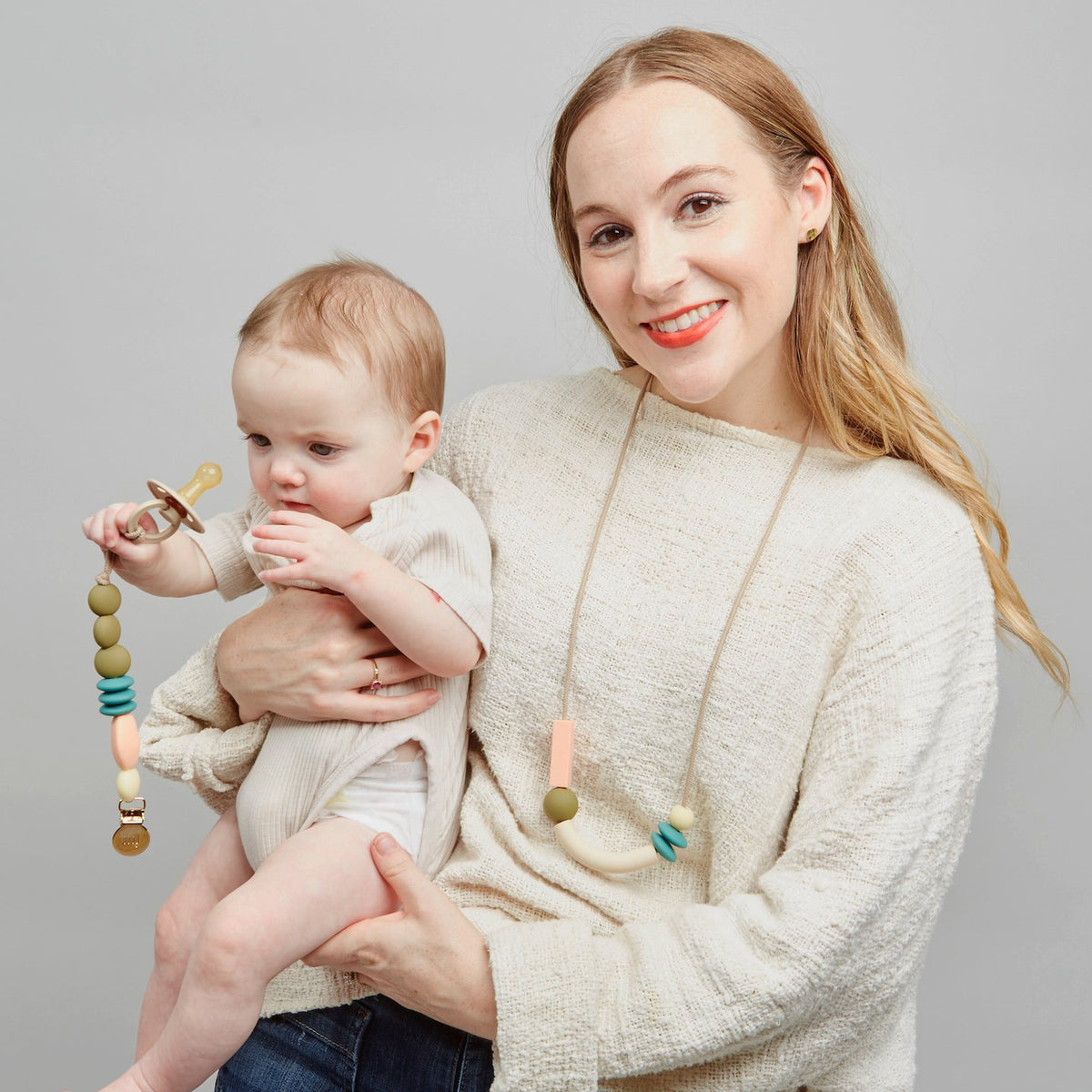Woman holding a baby with a teething toy against a gray background