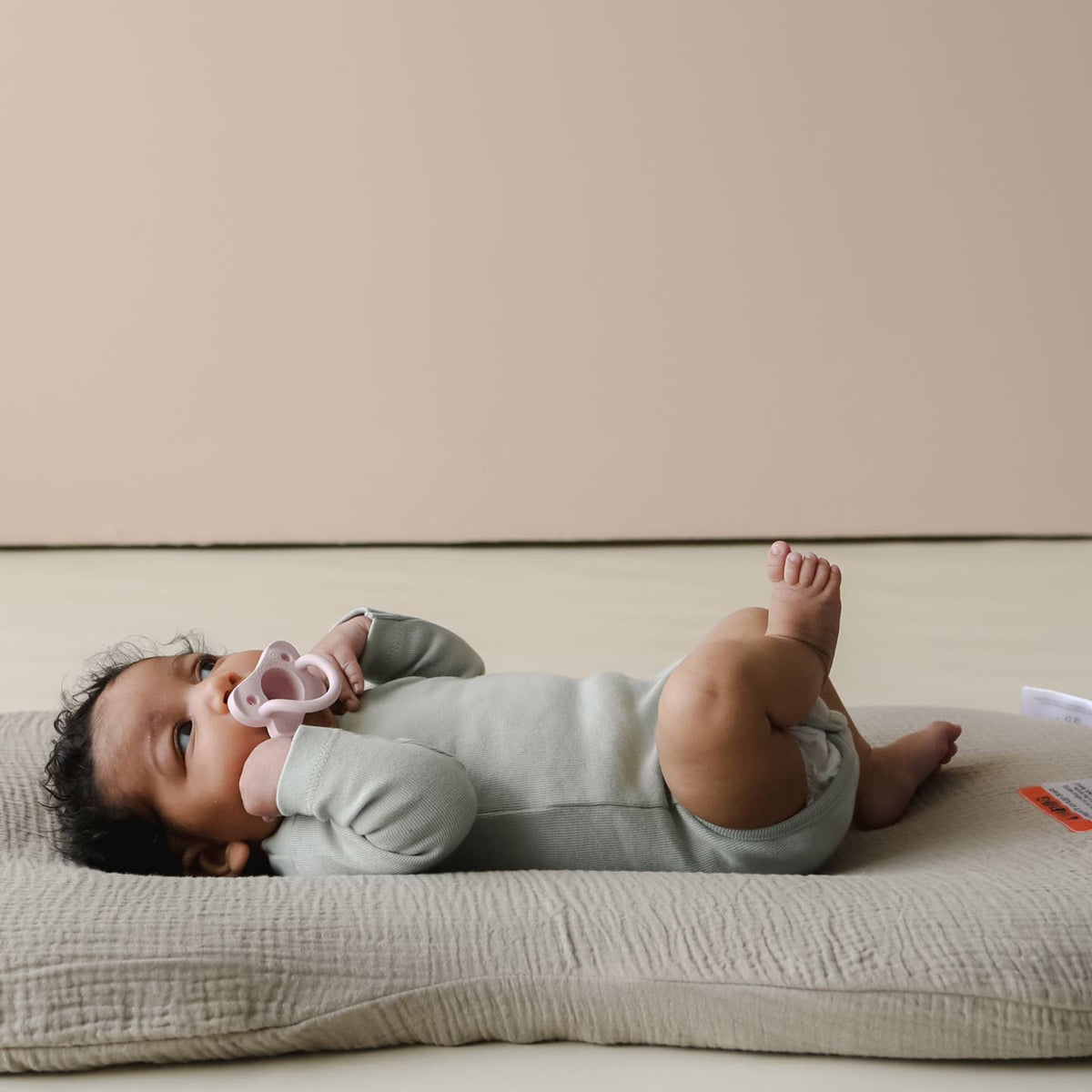 Baby lying on a beige surface with a pacifier in mouth
